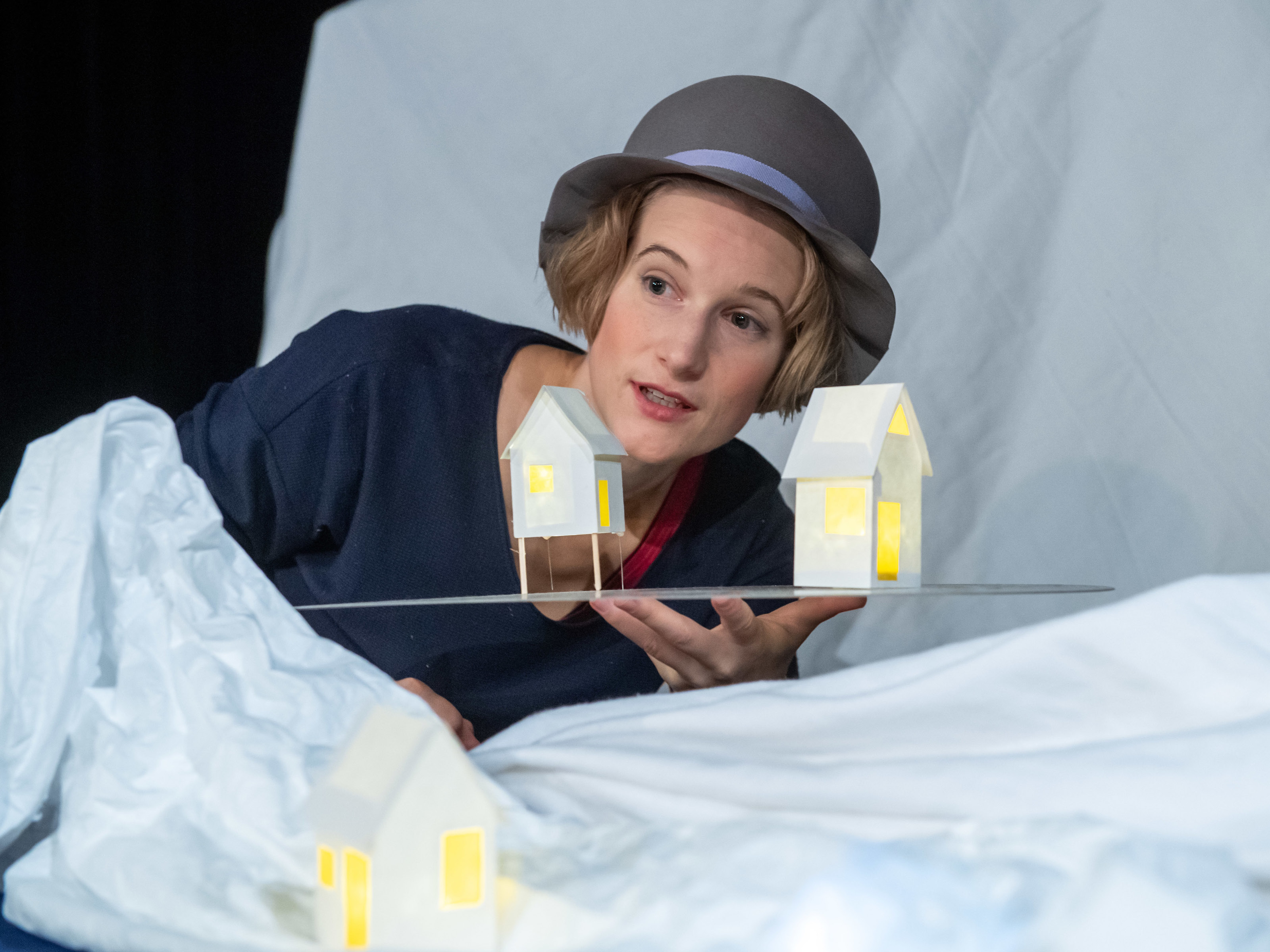 Figure player Miriam Hesse stands with a gray hat in a snowy landscape and holds two small houses on a plate in her hand. Warm light shines from the little houses.