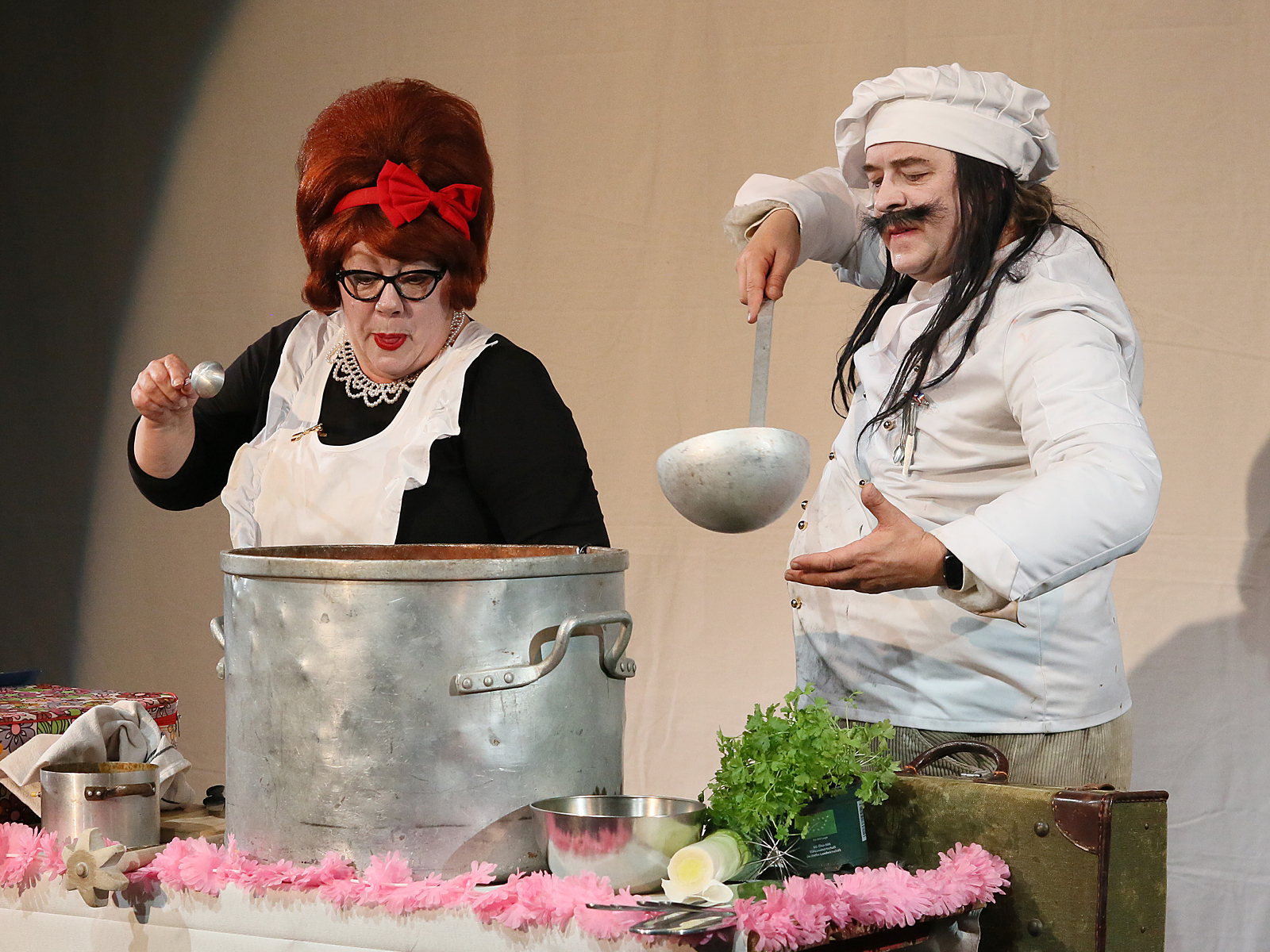 Koch und Köchin beugen sich über einen großen Topf.