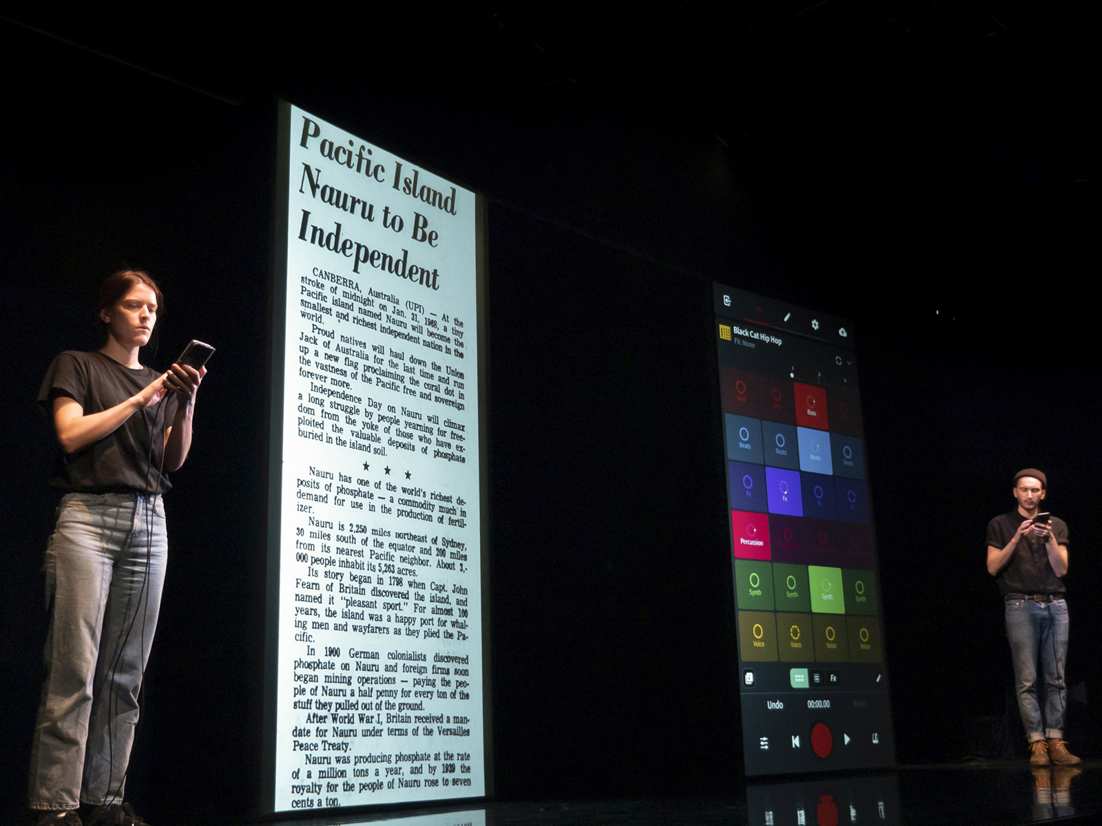 Zwei Menschen auf der Bühne, neben ihnen je übergroße Handy-Bildschirme, die als Projektionsflächen dienen.