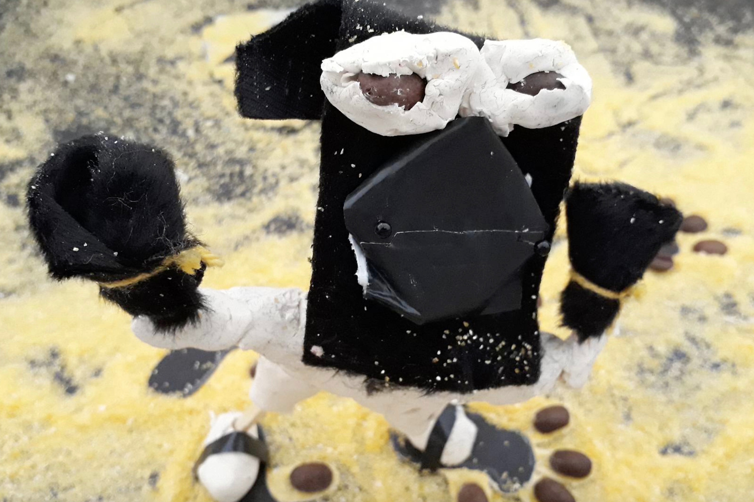 Aus schwarzer und weißer Pappe gebasteltes Monster auf gelbfarbigem Sand.