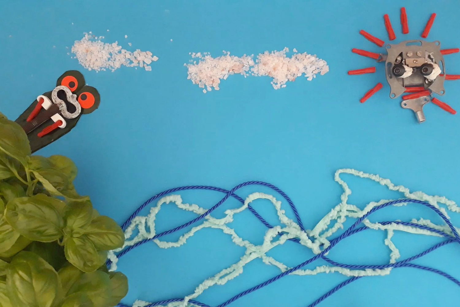 Collage mit Basilikum, Knete und Papier. Abgebildet ist ein kleines froschartiges Monster vor blauem Himmel.